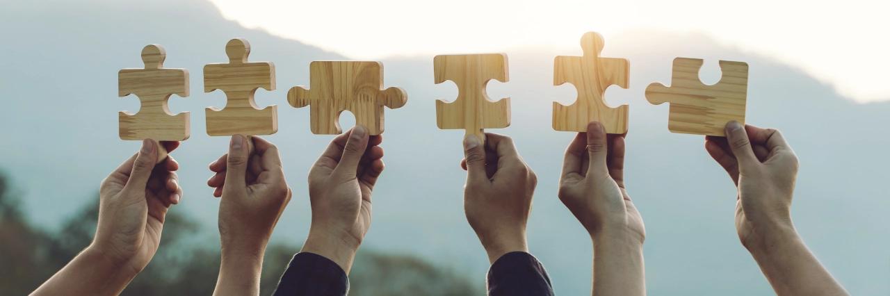 Sechs Hände halten verschiedene Puzzleteile aus Holz in Richtung Himmel