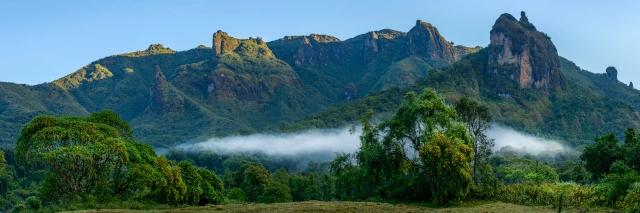Landschaft mit grünen Bäumen vor grünem Berghang unter blauem Himmel