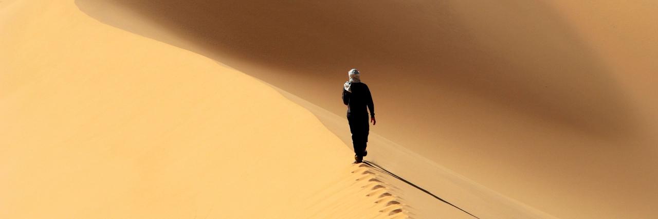Wanderer läuft auf einer Sanddüne mit Fußspuren hinter ihm im Sand