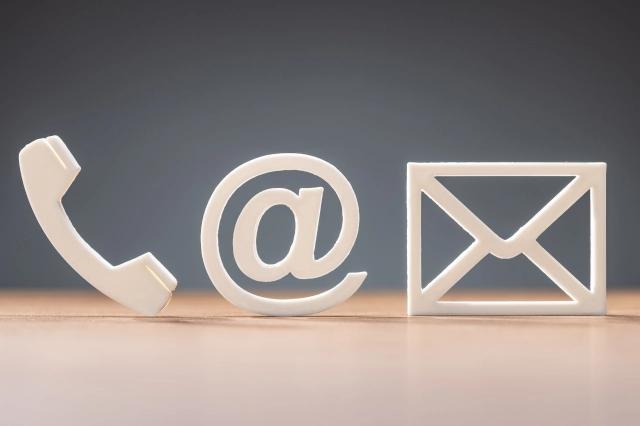 Weißer Schriftzug mit Telefonhörer, @-Zeichen und Brief steht auf Holzplatte vor blauer Wand