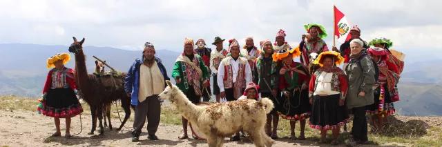 13 Personen der Cuyuni Gemeinde aus Peru stehen aufgereiht mit zwei Lamas nebeneinander und lächeln freundlich