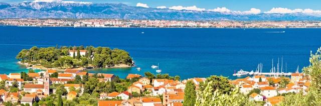 Stadt an der Küste am blauen Meer mit Bergen im Hintergrund unter blauem Himmel