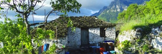Eine einfache, weiße Hütte aus Ziegeln mit einem braunen Dach. Im Hintergrund sind Berge.