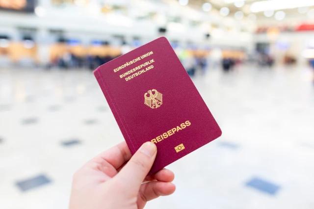 Eine Hand hält einen deutschen Reisepass in einem Flughafenterminal