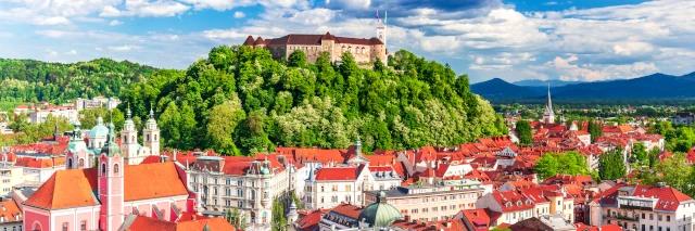 Luftaufnahme einer Stadt mit weißen Häusern und roten Dächern und einem grünen Hügel mit einem Schloss
