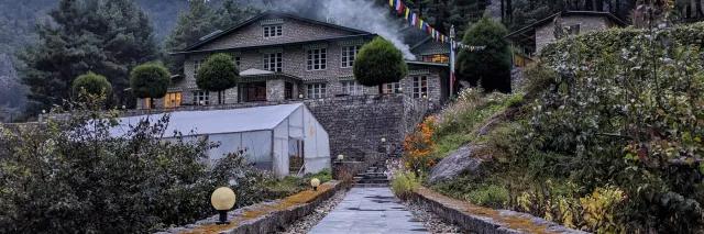 Frontale Sicht auf einen Weg der zu einer typischen Loge in Nepal mit Gebetsfahnen führt