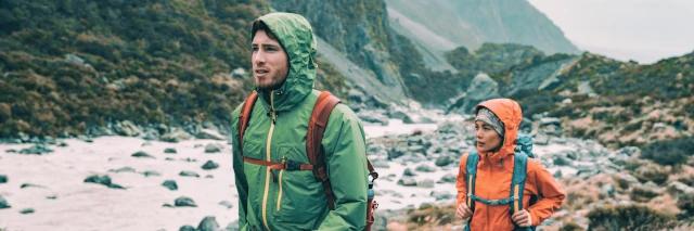Ein Mann und eine Frau mit Rucksäcken und Regenkleidung in einer Bergumgebung