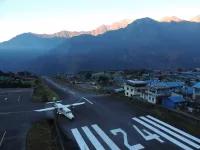 Landebahn mit einem Flugzeug und Häusern vor Bergkulisse im Hintergrund