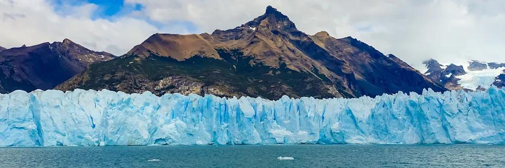 Perito-Moreno-Gletscher vor einem See und Bergkulisse im Hintergrund bei bewölktem Himmel