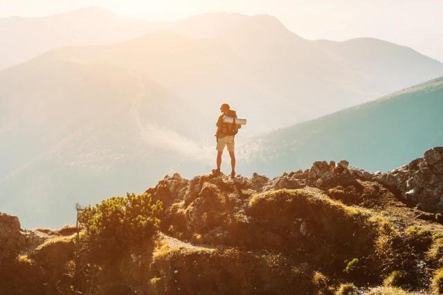 Wanderer mit Rucksack steht auf dem Berg und blickt in die Weite