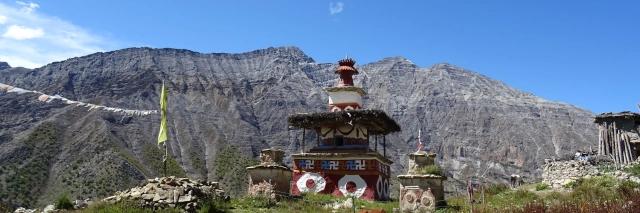 Ein religiöses Bauwerk steht auf einem Hügel mit Bergen im Hintergrund unter blauem Himmel