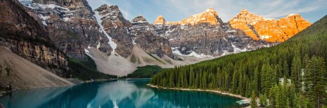 Ein tiefblauer See umrandet von Bergen und Wäldern. Die Berge sind teils schneebedeckt.