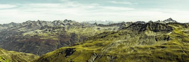 Panorama einer grünen Berglandschaft mit gezackten Gipfeln unter bewölktem Himmel