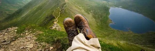 Füße mit Wanderschuhen auf dem Berggipfel mit Blick auf grüne Berglandschaft und blauen See