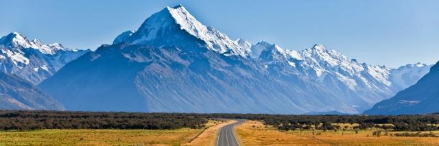 Straße führt auf eine schneebedeckte Bergkette zu mit einem hohen Berg in der Mitte