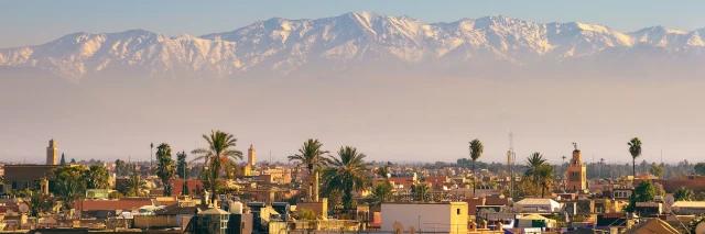 Blick über Marrakesch mit Aussicht zum Atlas Gebirge. Es hängt ein leichter Nebel über Stadt.