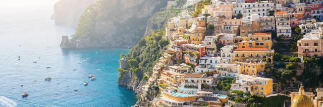 Blick auf eine kleine am Hang gebaute Stadt. Der Hang beginnt direkt neben dem Meer, auf dem kleine Boote zu sehen sind.