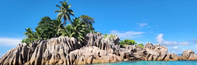 Blick auf eine kleine Felseninsel. Die Insel ist mit Palmen bewachsen.