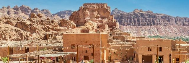 Antike Stadt mit Steinburg vor einer Felsenkette unter blauem Himmel