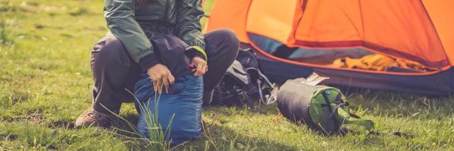 Eine Frau sitzt vor ihrem Zelt und räumt ihren Schlafsack auf.