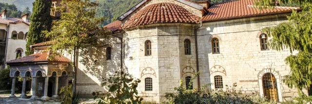 Klosterkomplex von außen mit Ziegeldächern und grünem Vorgarten mit Pflanzen und Bäumen