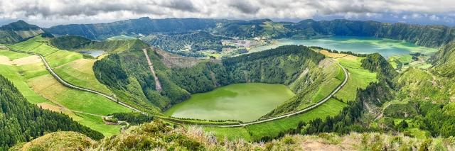 In einem Krater ist ein grün scheinender See. Dahinter sieht man einen weiteren See und ein Dorf.