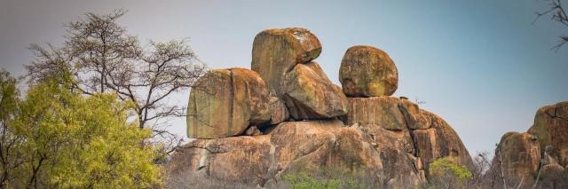 Formation von mehreren großen Felsbrocken übereinander hinter vereinzelten Bäumen