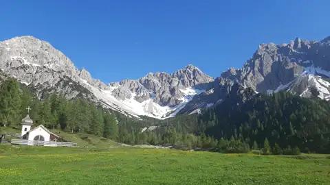 Alpenlandschaft mit Hütte und schneebedeckten Gipfeln.