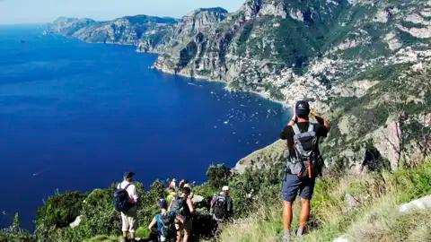 Wanderer mit Rucksäcken auf einem Bergpfad mit Blick auf die Küste und das tiefblaue Meer.