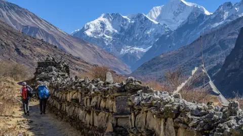 Wanderer auf einem Bergpfad mit Blick auf schneebedeckte Gipfel.