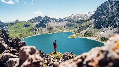 Wanderer mit Blick auf einen türkisblauen Bergsee in den Alpen.