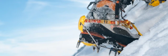Ein Fuß mit Wanderschuh und Steigeisen steckt im Schnee