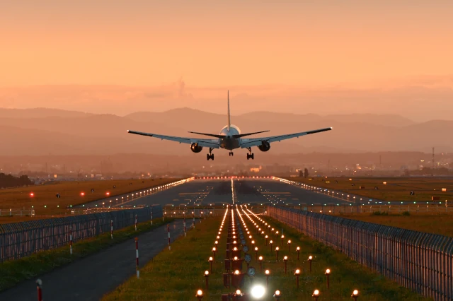 Flugzeug hebt auf beleuchteter Landebahn ab in einer orangenen Lichtstimmung am Abend