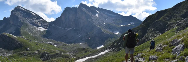 Blick auf zwei Wanderer, die auf steinigen schmalen Pfaden durch die karge Bergwelt Albaniens gehen. 