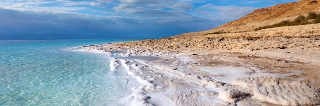 Türkisblaues Wasser, Strand mit weißem Sand und helle, flache Felsenküste unter blauem Himmel