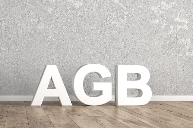 Schriftzug mit AGB steht auf Holzboden vor grauer Wand und weißer Bodenleiste