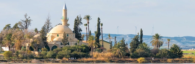 Moschee am Wasser umrundet von grüner Vegetation unter bewölktem Himmel