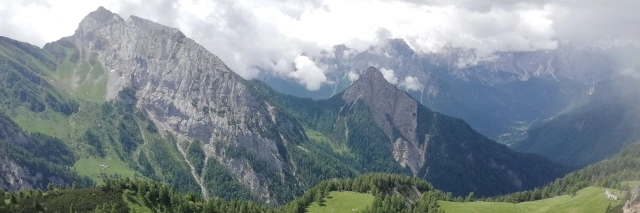 Blick auf die felsige Hügellandschaft der karnischen Alpen, über denen weiße Wolken schweben. 