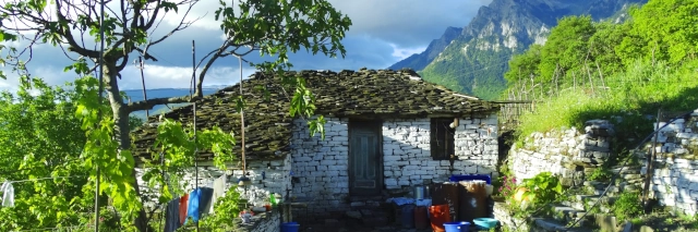 Eine einfache, weiße Hütte aus Ziegeln mit einem braunen Dach. Im Hintergrund sind Berge.