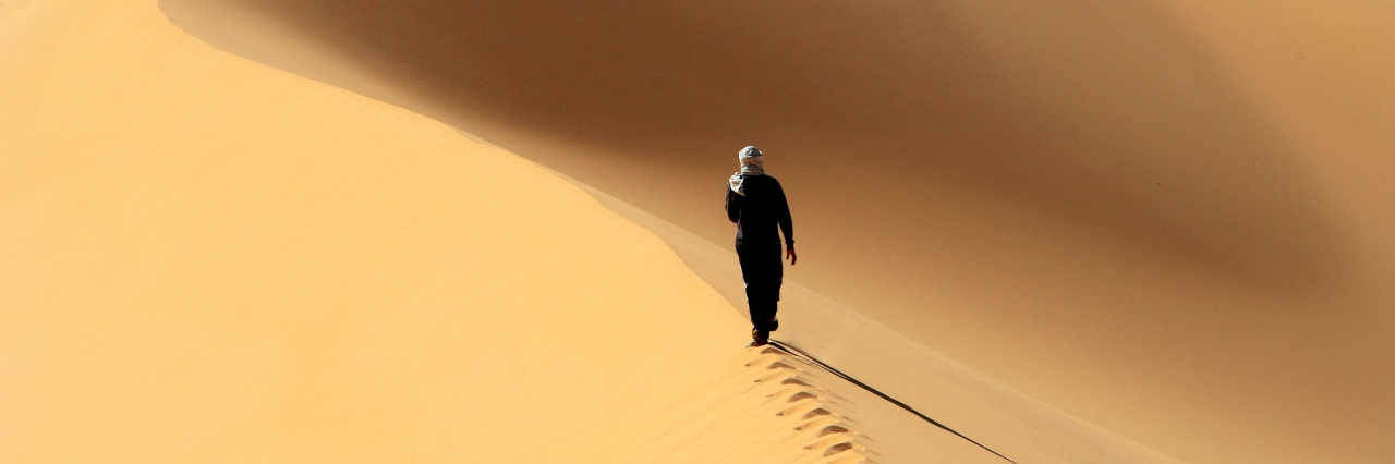 Wanderer läuft auf einer Sanddüne mit Fußspuren hinter ihm im Sand