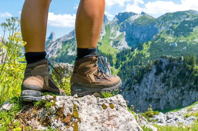 Zwei Füße mit Wanderschuhen sind in Nahaufnahme auf felsigem Untergrund zu sehen. 