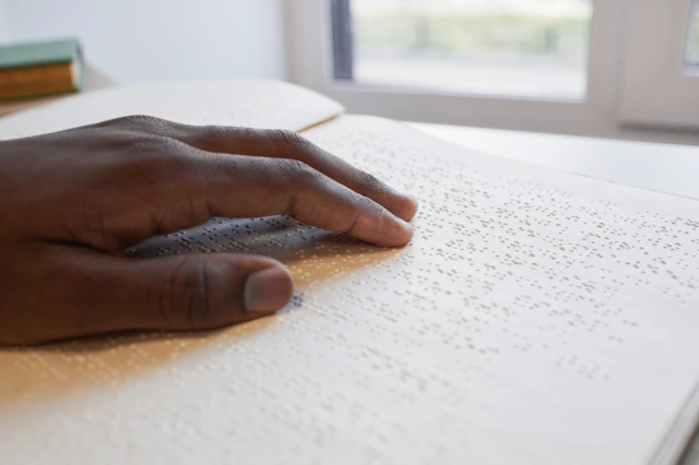 Nahaufnahme einer Hand, die in einem Buch Blindenschrift liest.