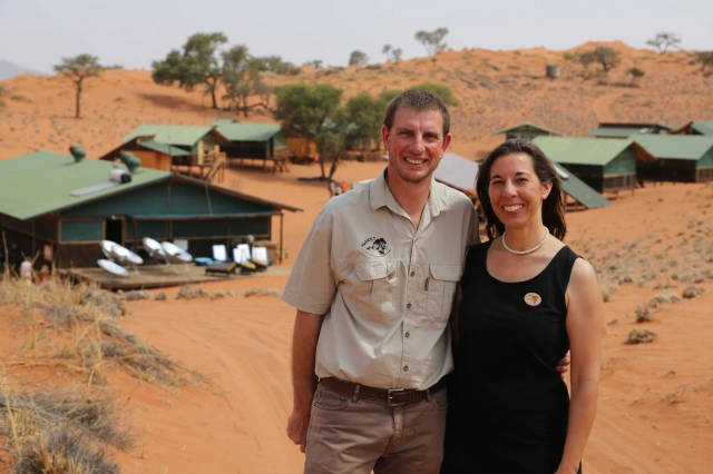 Viktoria und Andreas Keding, Gründer von NaDEET, stehen Arm in Arm vor mehreren Gebäuden in einer kargen Wüstenlandschaft. 