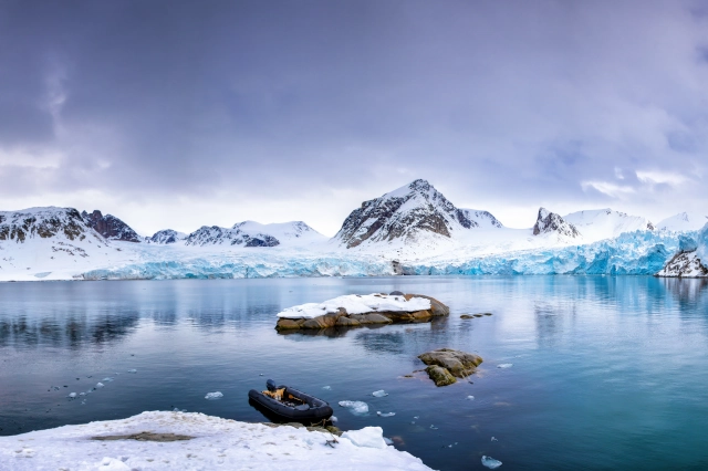 Ein blaues Gewässer. Ringsum sind Eisschollen, Gletscher und schneebedeckte Berge. 