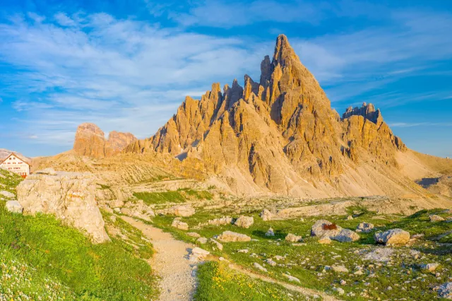 Wanderweg führt vorbei an Wiesen auf Berge im Abendlicht zu unter leicht bewölktem Himmel