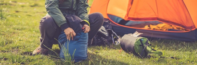 Eine Frau sitzt vor ihrem Zelt und räumt ihren Schlafsack auf. 