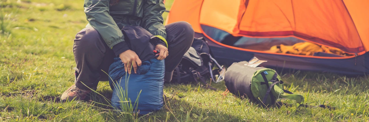 Eine Frau sitzt vor ihrem Zelt und räumt ihren Schlafsack auf. 