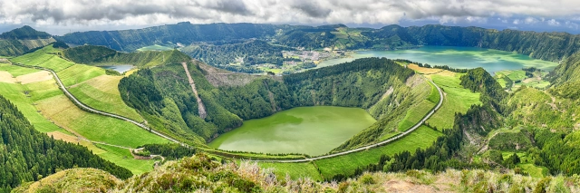 In einem Krater ist ein grün scheinender See. Dahinter sieht man einen weiteren See und ein Dorf.