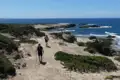Zwei Wanderer auf einem Küstenpfad. Das Meer und felsige Küstenabschnitte sind im Hintergrund sichtbar.