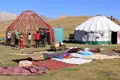 Aufbau einer Jurte in den Bergen. Mehrere Personen arbeiten zusammen, um das Gerüst der Jurte zu errichten. Im Hintergrund ist eine fertig aufgebaute Jurte zu sehen.